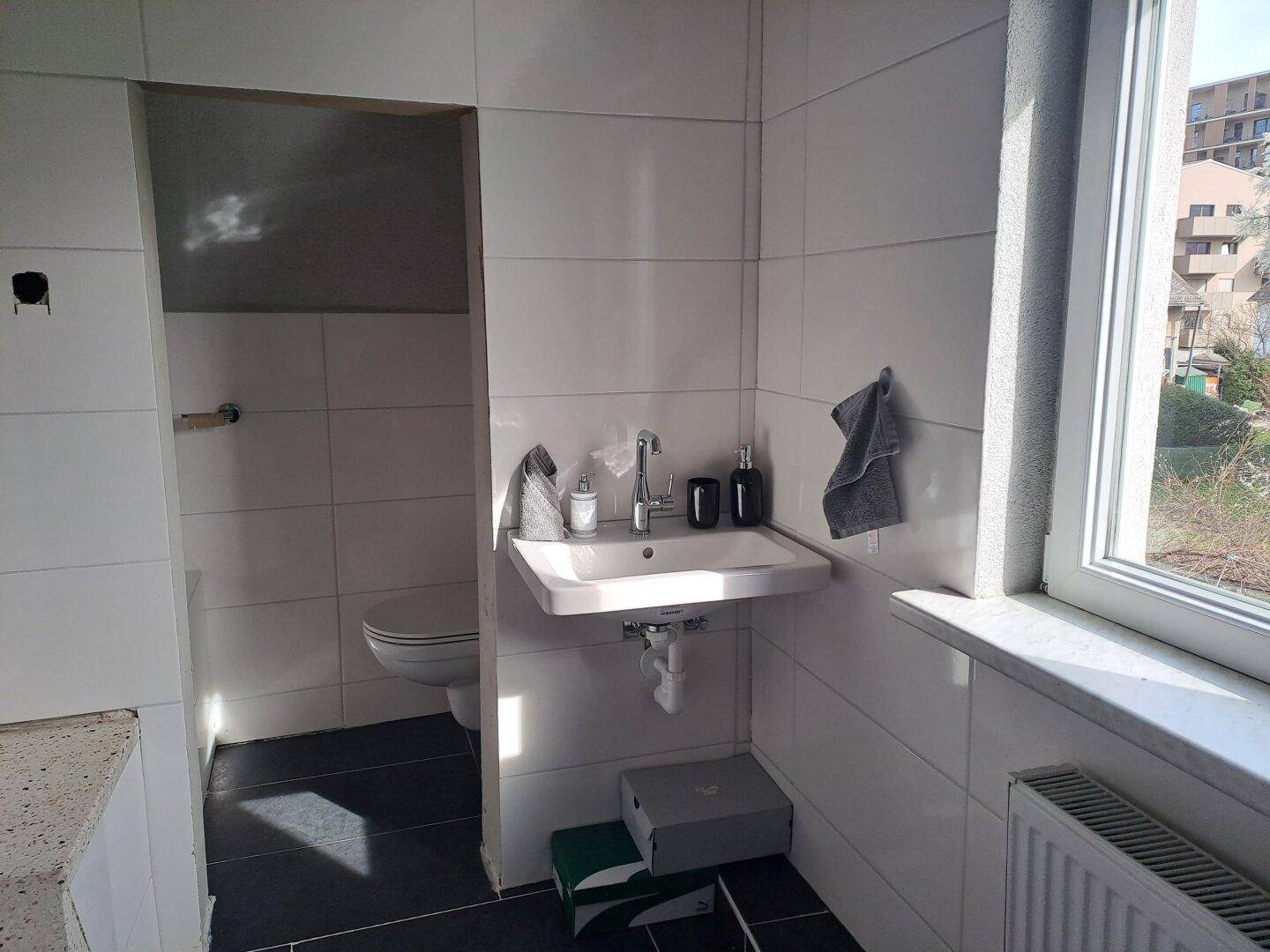 Helles WC mit Waschbecken, Toilette und Fenster für Tageslicht.