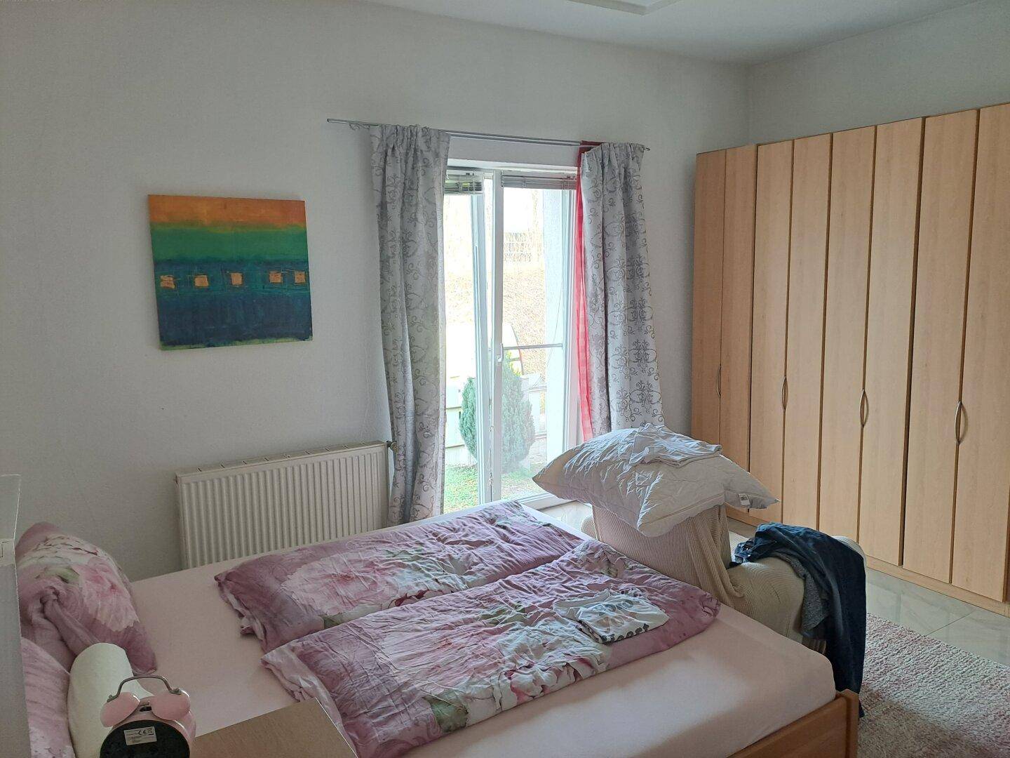 Schlafzimmer mit Doppelbett, Holzschrank und Zugang zum Garten oder Balkon.