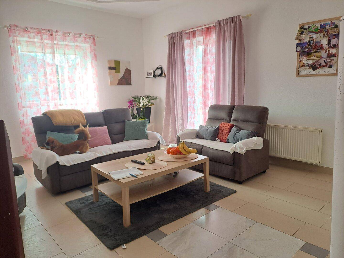 Gemütliches Wohnzimmer mit zwei Sofas, Couchtisch und hellen Vorhängen.