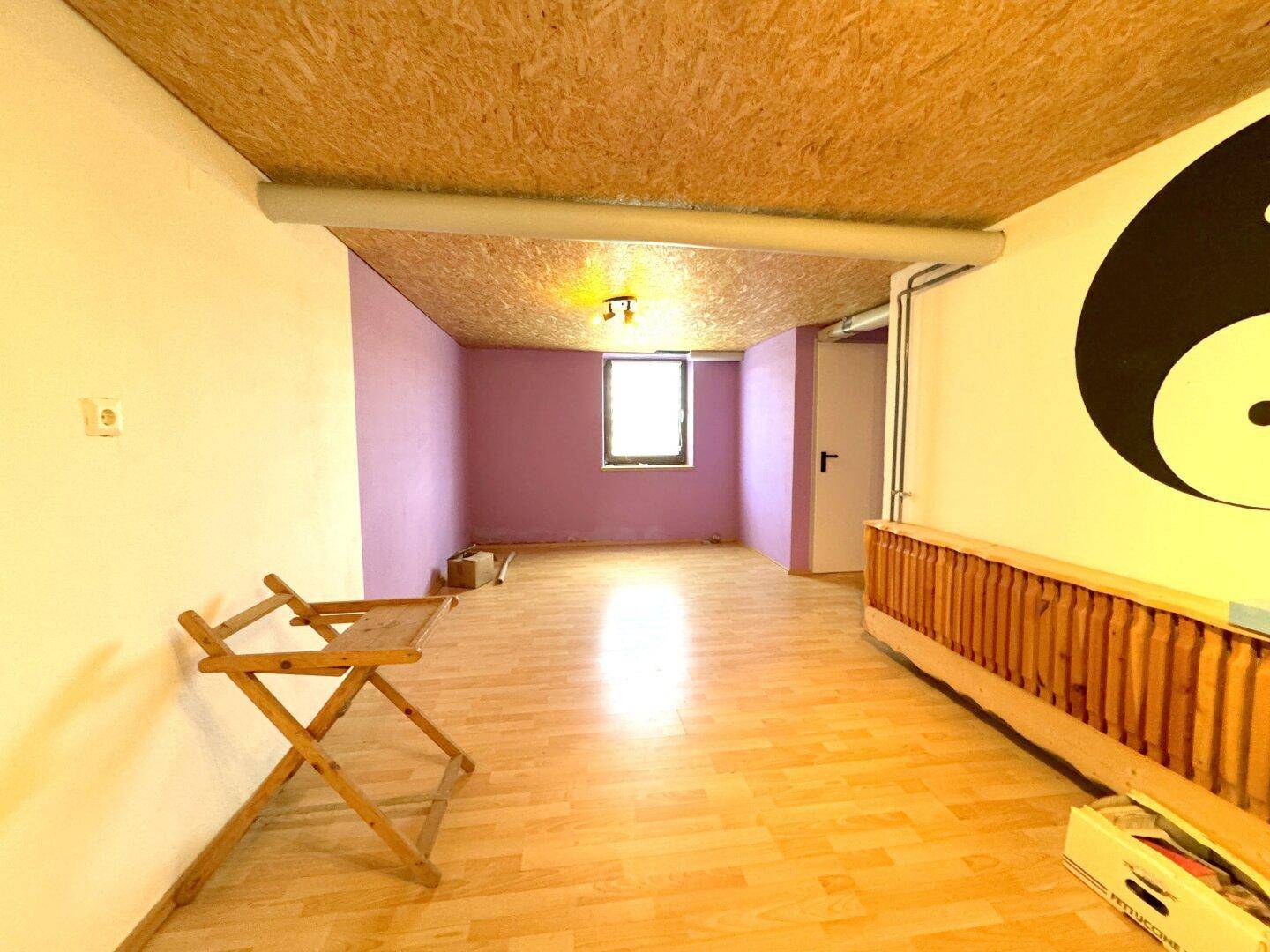Geräumiger Kellerraum mit OSB-Decke, Holzboden und lila gestrichenen Wänden.