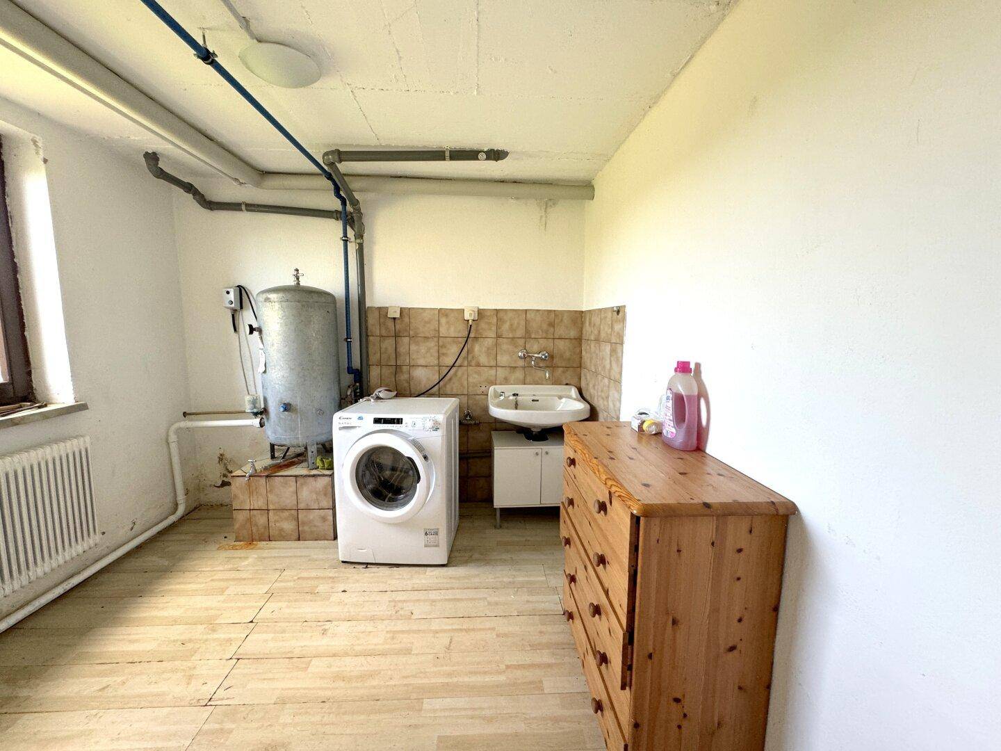 Funktionaler Hauswirtschaftsraum mit Waschmaschine, Warmwasserboiler und Waschbecken.