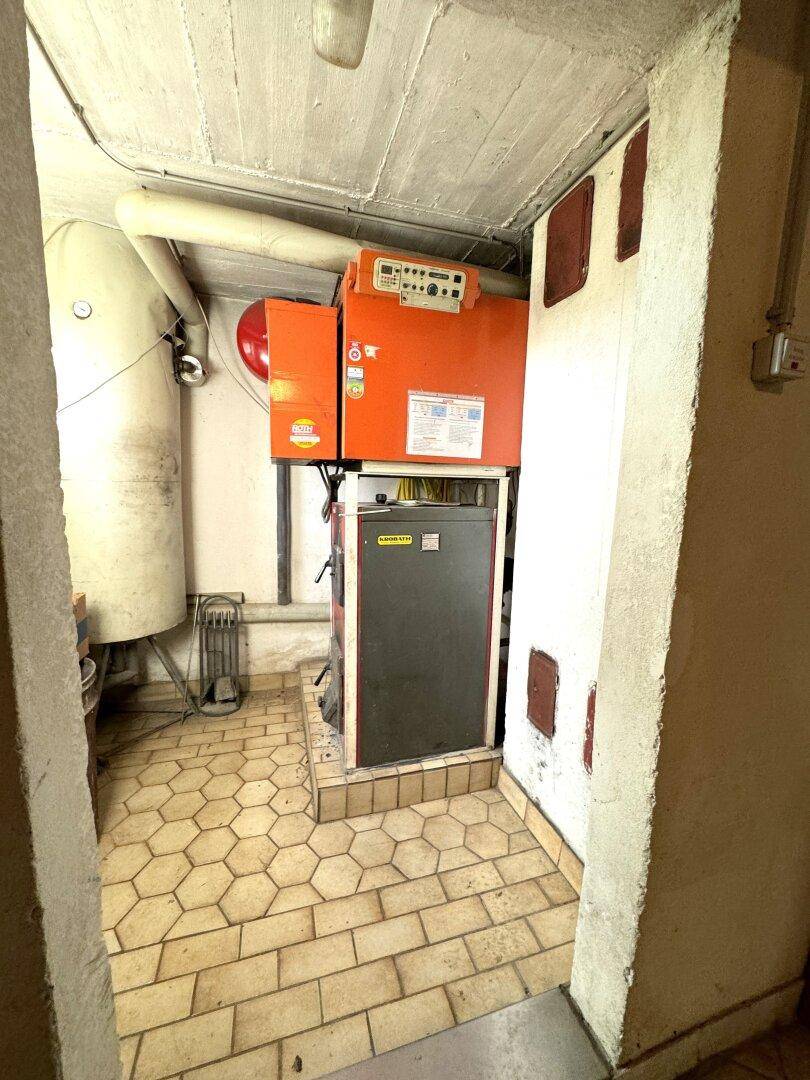 Heizungsraum mit großem Boiler und Heizungsanlage auf sechseckigen Fliesen.