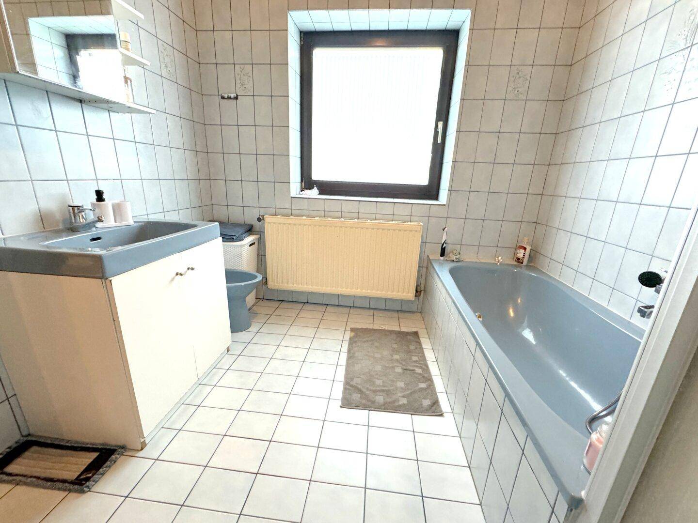 Badezimmer mit blauer Badewanne, Fliesen und Fenster für natürliches Licht.
