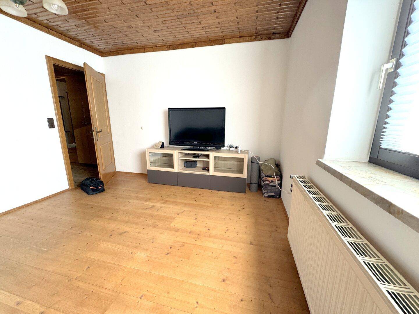 Wohnzimmer mit Holzbalkendecke, Holzboden und einem Fernsehschrank.