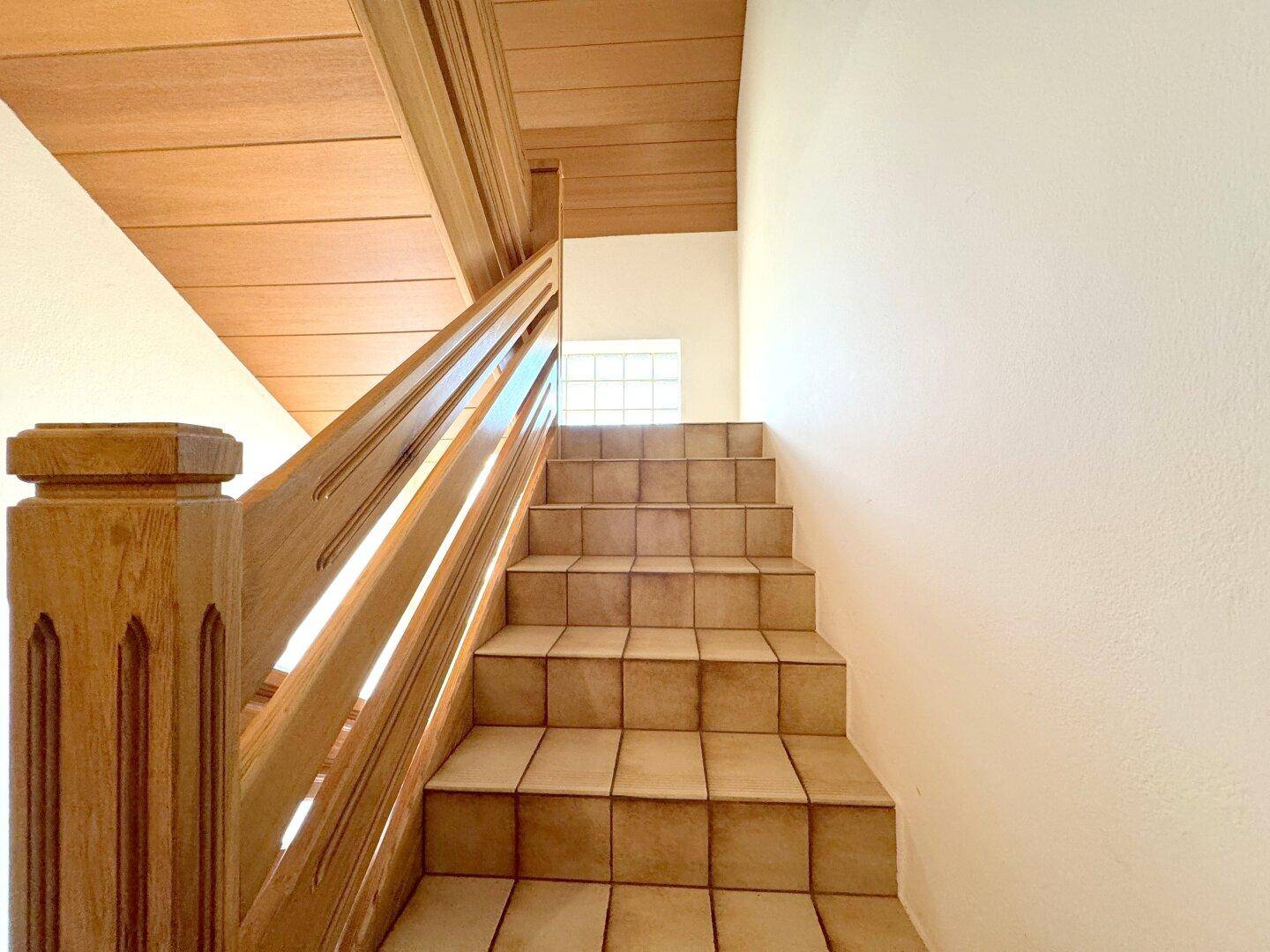 Treppenhaus mit Holzgeländer und gefliesten Stufen, das in die obere Etage führt.