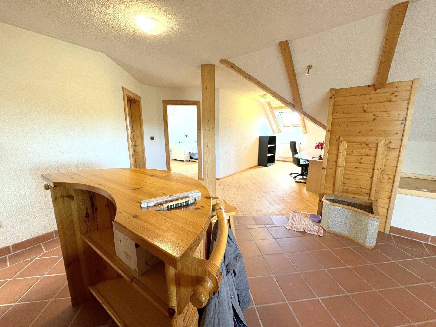 Geräumiger Dachgeschossbereich mit Holzbalken, Terrakottafliesen und einem Barbereich.