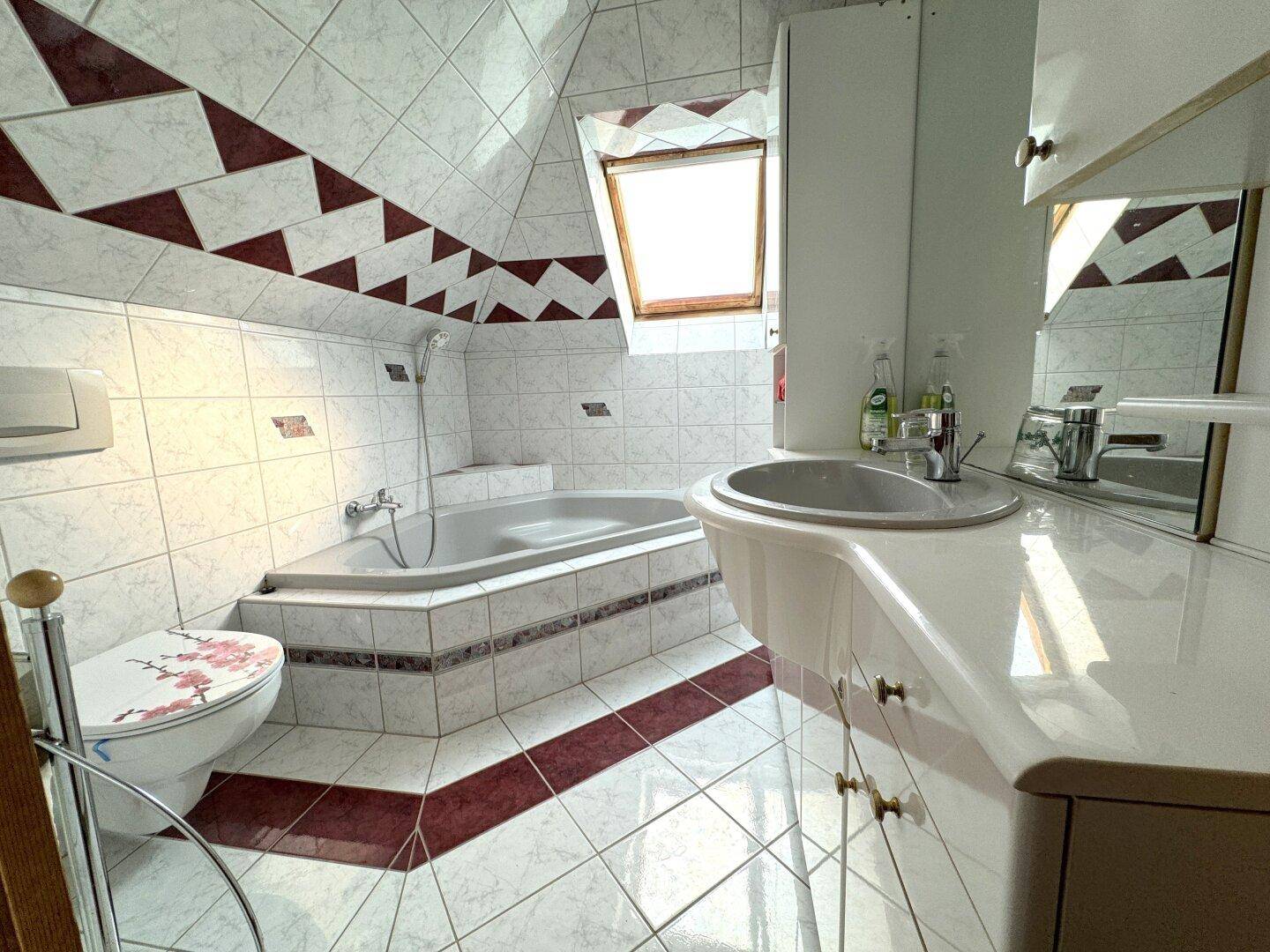 Badezimmer im Dachgeschoss mit Eckbadewanne, Fliesen und Dachfenster.