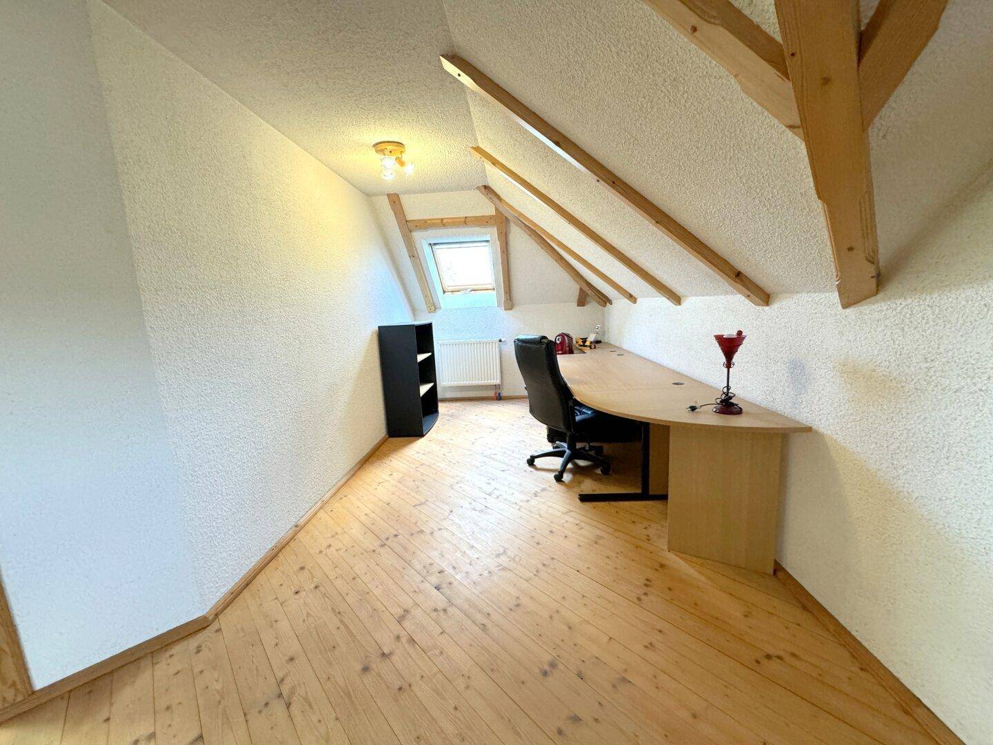 Dachgeschossbüro mit Holzboden, Dachfenster und einem langen Schreibtisch.