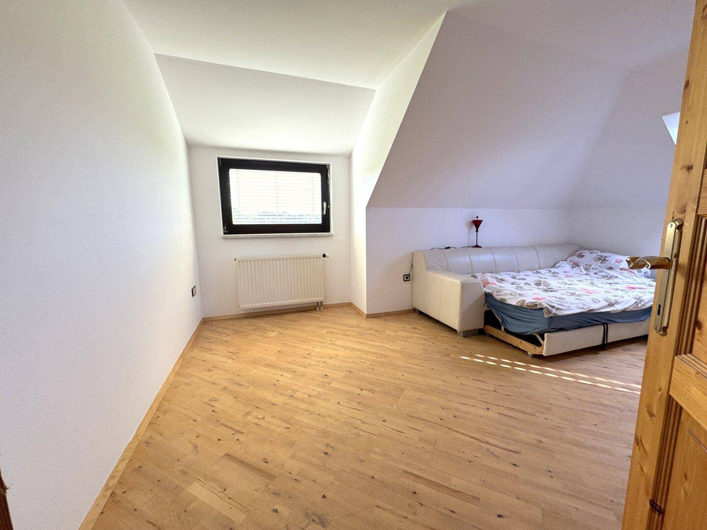 Helles Schlafzimmer im Dachgeschoss mit Holzboden und einem großen Fenster.