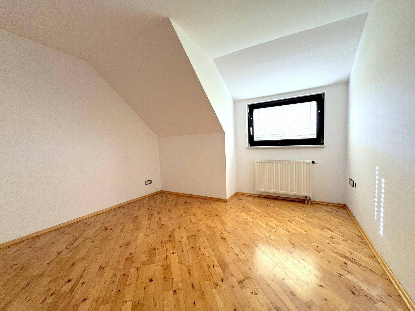 Schlafzimmer im Dachgeschoss mit Holzboden, weißen Wänden und viel Tageslicht.