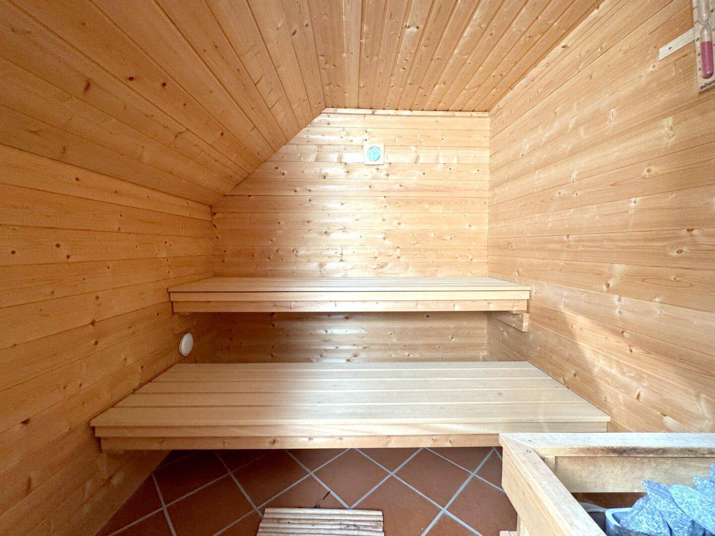 Holzvertäfelte Sauna mit zwei Bänken und Terrakottafliesen auf dem Boden.
