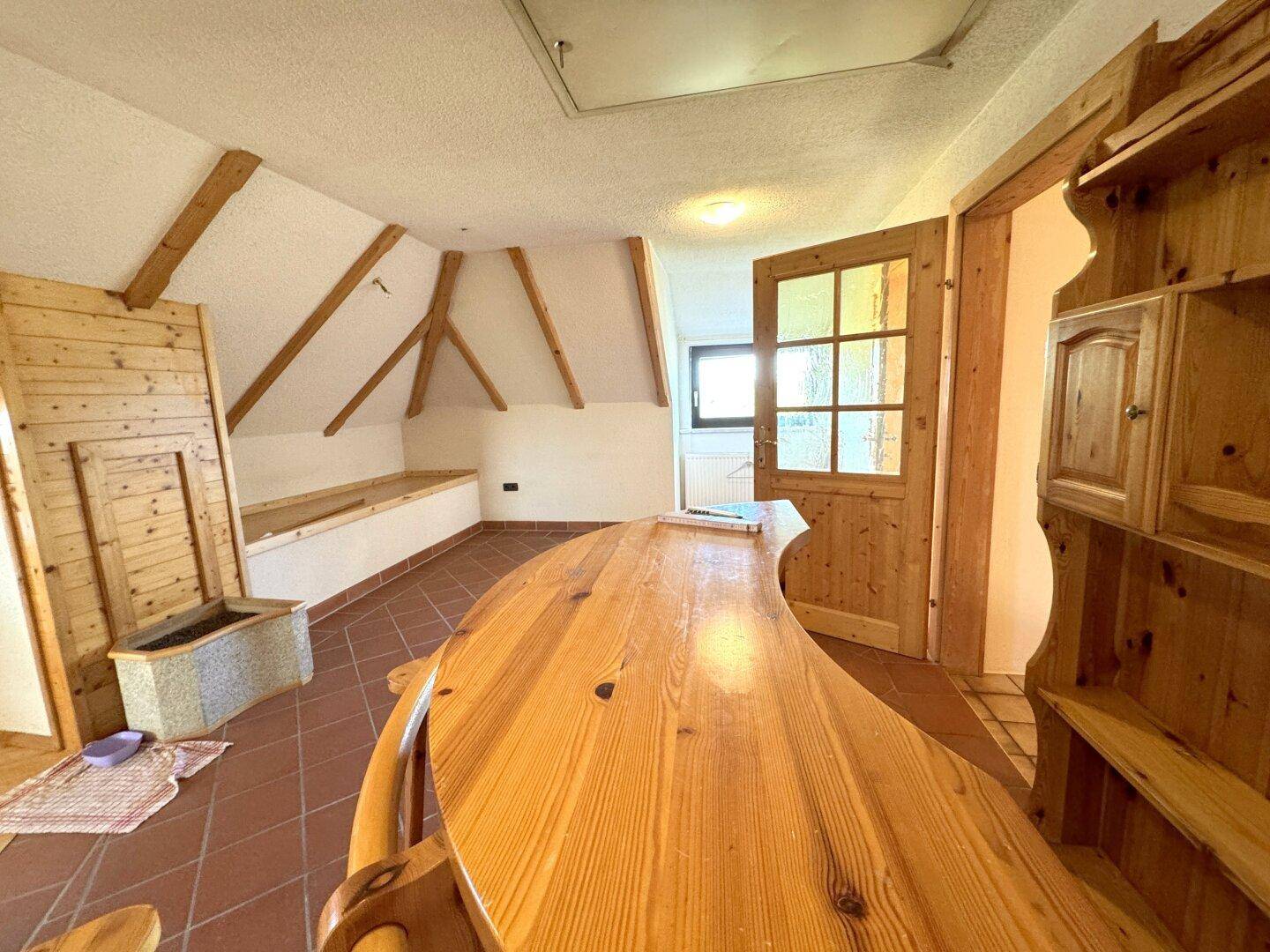 Dachgeschossraum mit Holzbalken, Terrakottafliesen und rustikalen Holzmöbeln.