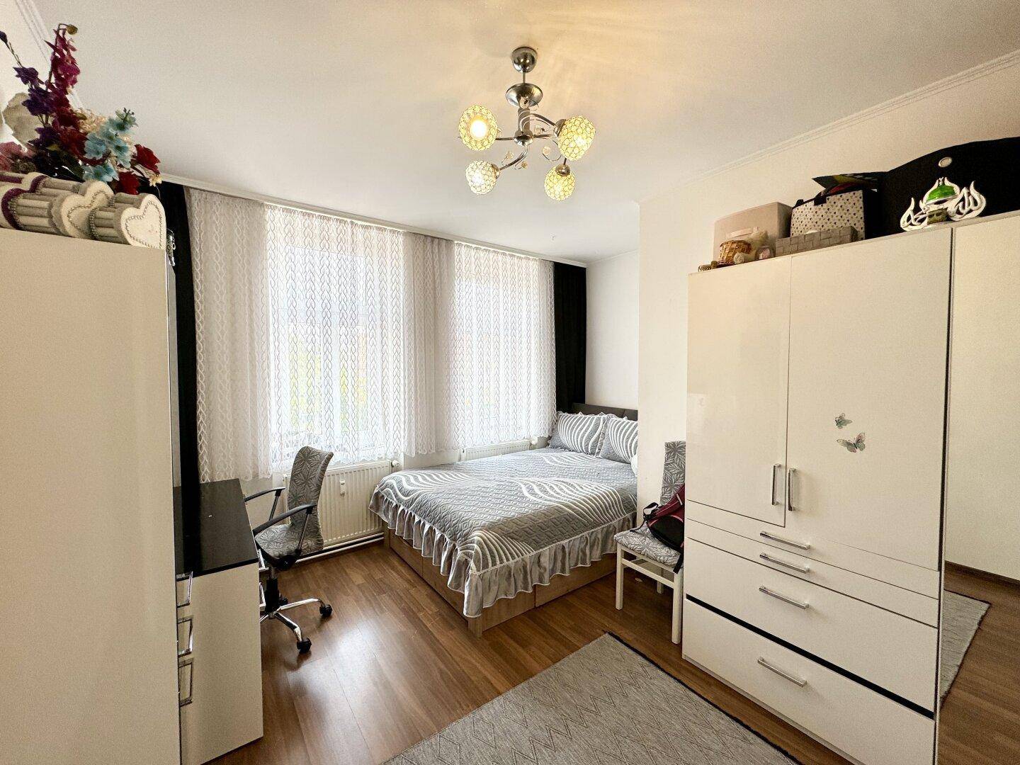 Helles Schlafzimmer mit Doppelbett, Kleiderschrank und Schreibtisch, ausgestattet mit Holzfußboden.