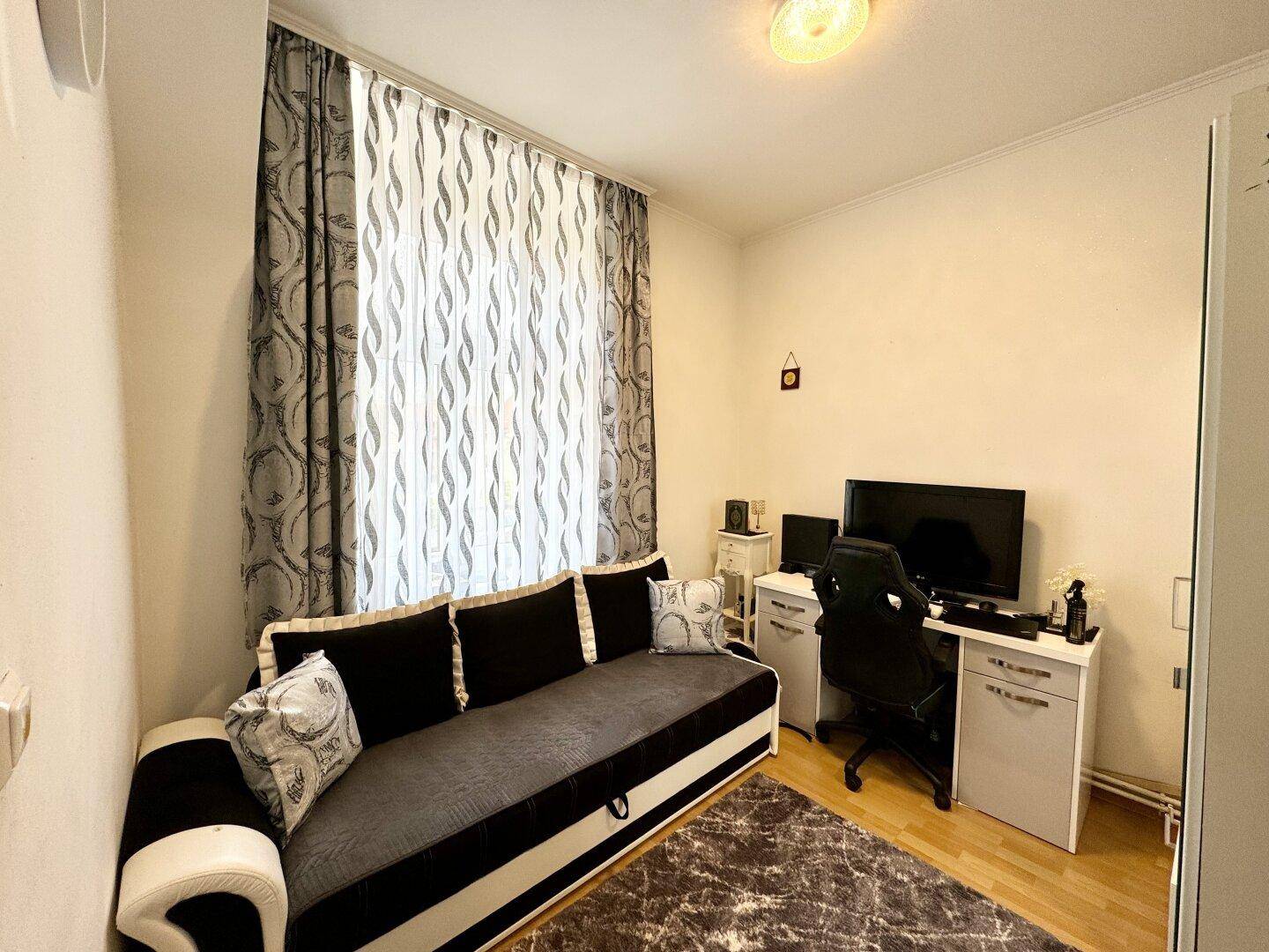 Gemütlicher Raum mit Schlafsofa, Schreibtisch und Computer-Setup, ideal als Gäste- oder Arbeitszimmer.