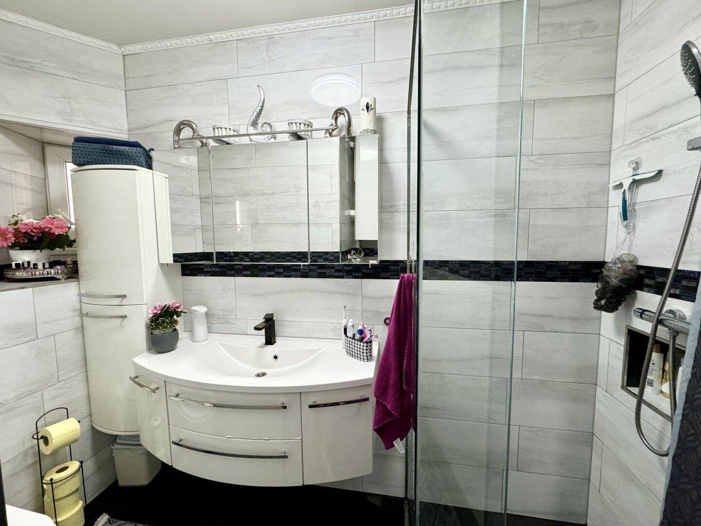 Modernes Badezimmer mit Duschkabine, Einzelwaschbecken und hellen Fliesen an den Wänden.