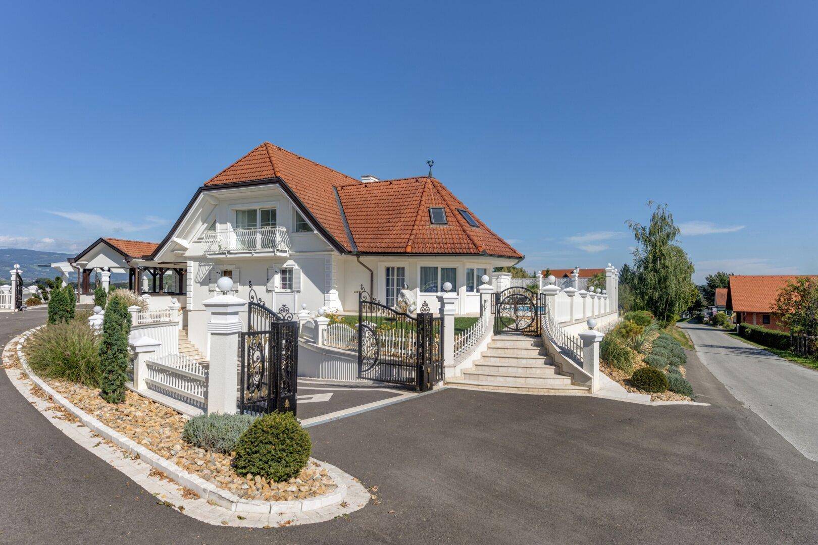 Elegantes Einfamilienhaus mit gepflegter Auffahrt, schmiedeeisernem Tor und klassischer Architektur.