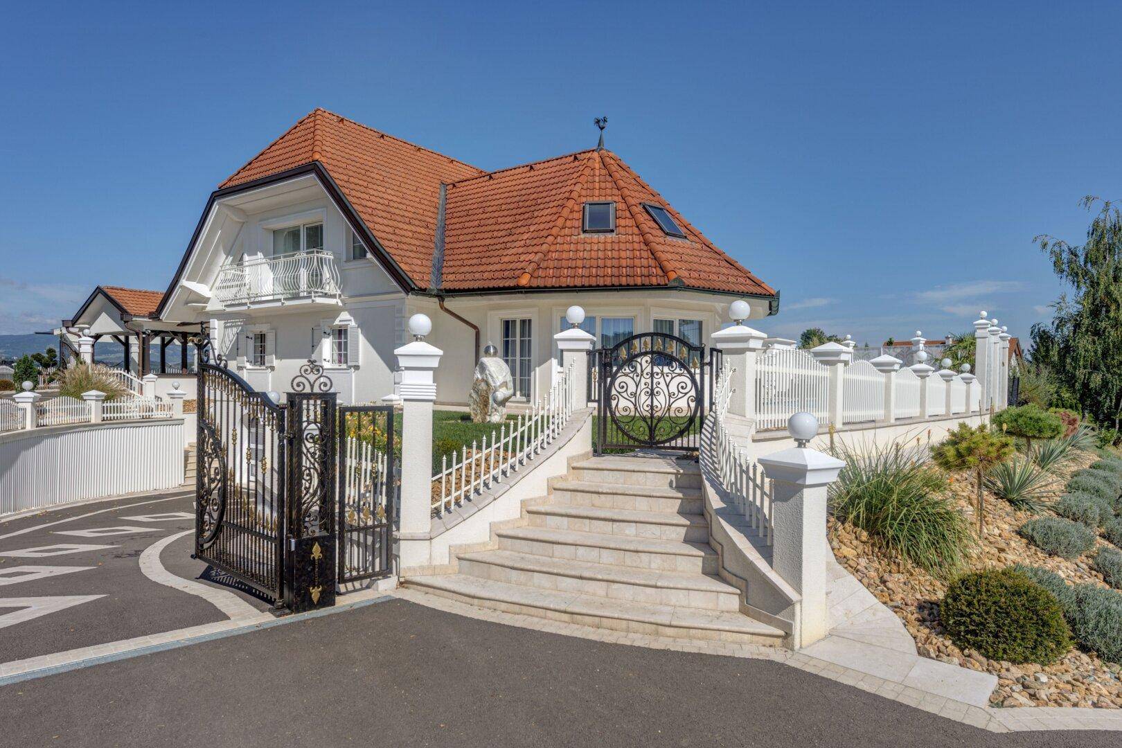 Herrschaftliches Anwesen mit großem Eingangstor, breiter Treppe und gepflegter Gartenanlage.