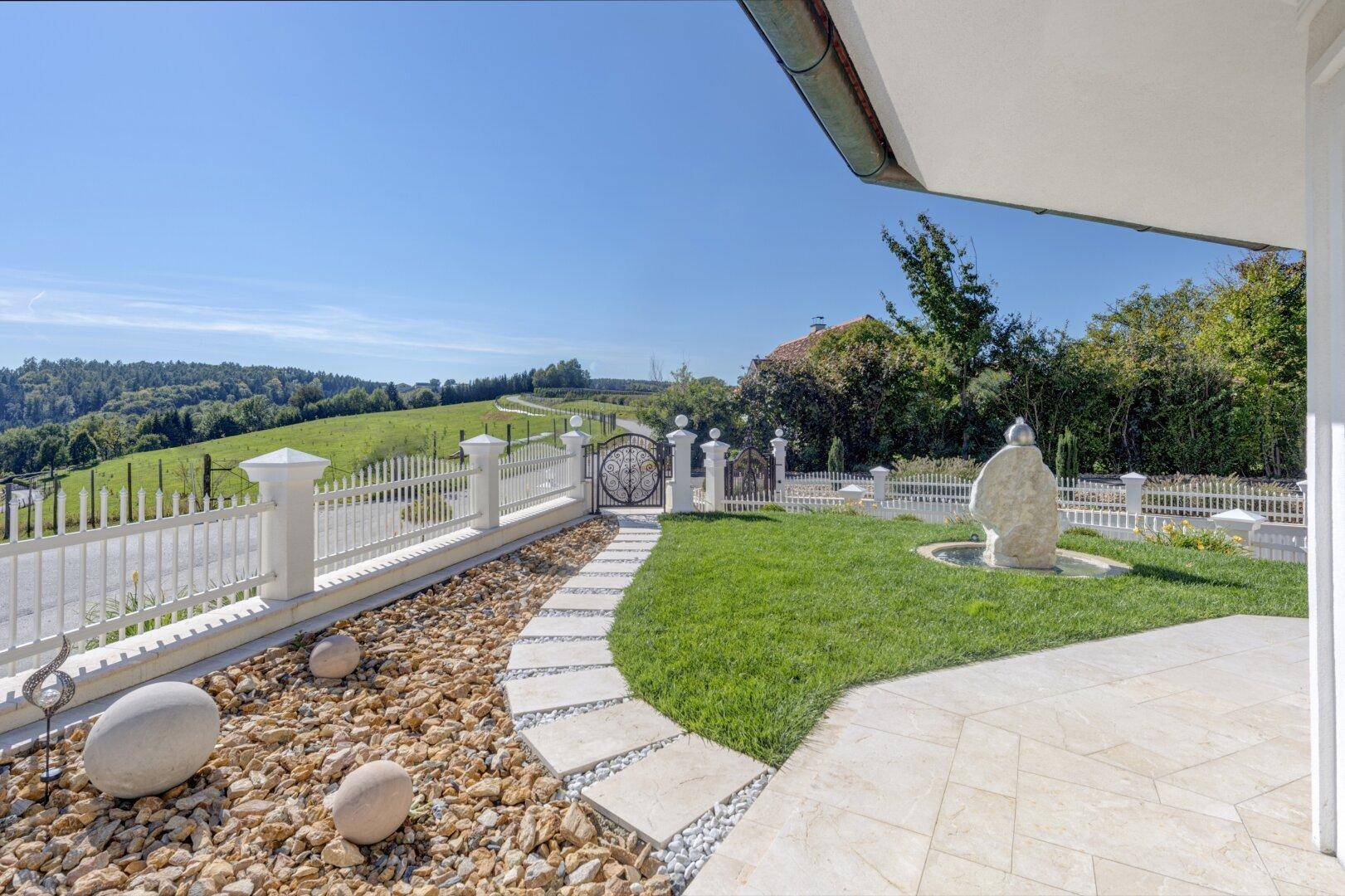 Gartenweg mit Trittplatten und Ziersteinen, führt zu einem Tor mit Blick auf die Landschaft.