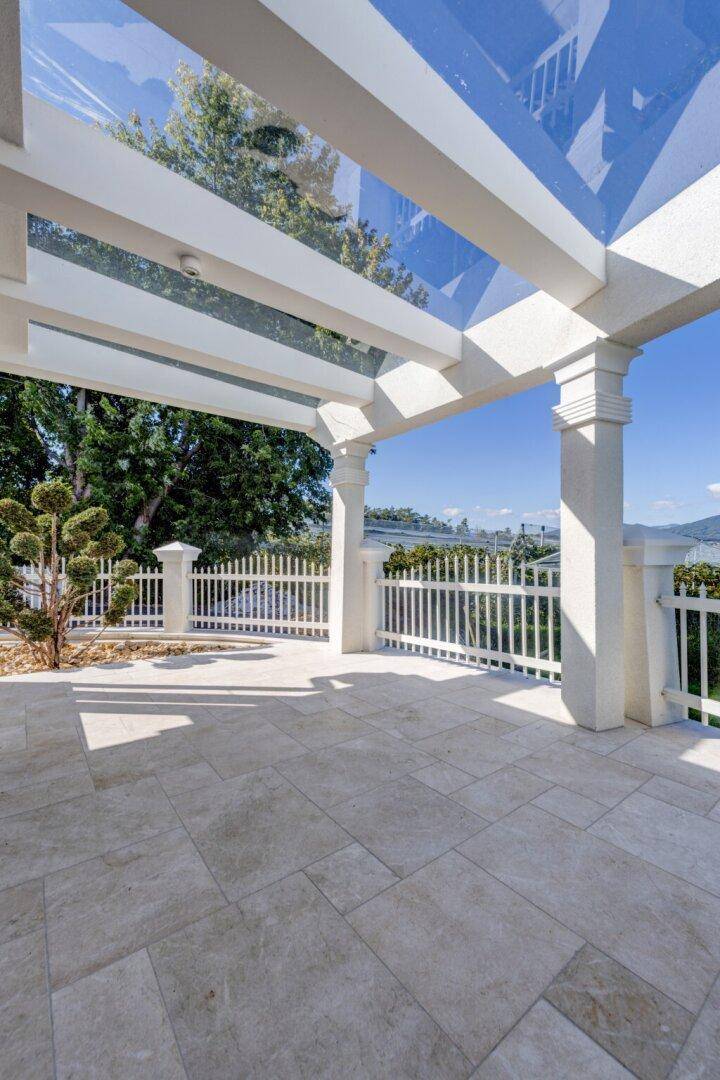 Überdachte Terrasse mit Glasdach und hellen Fliesen, bietet einen weiten Blick in die Landschaft.