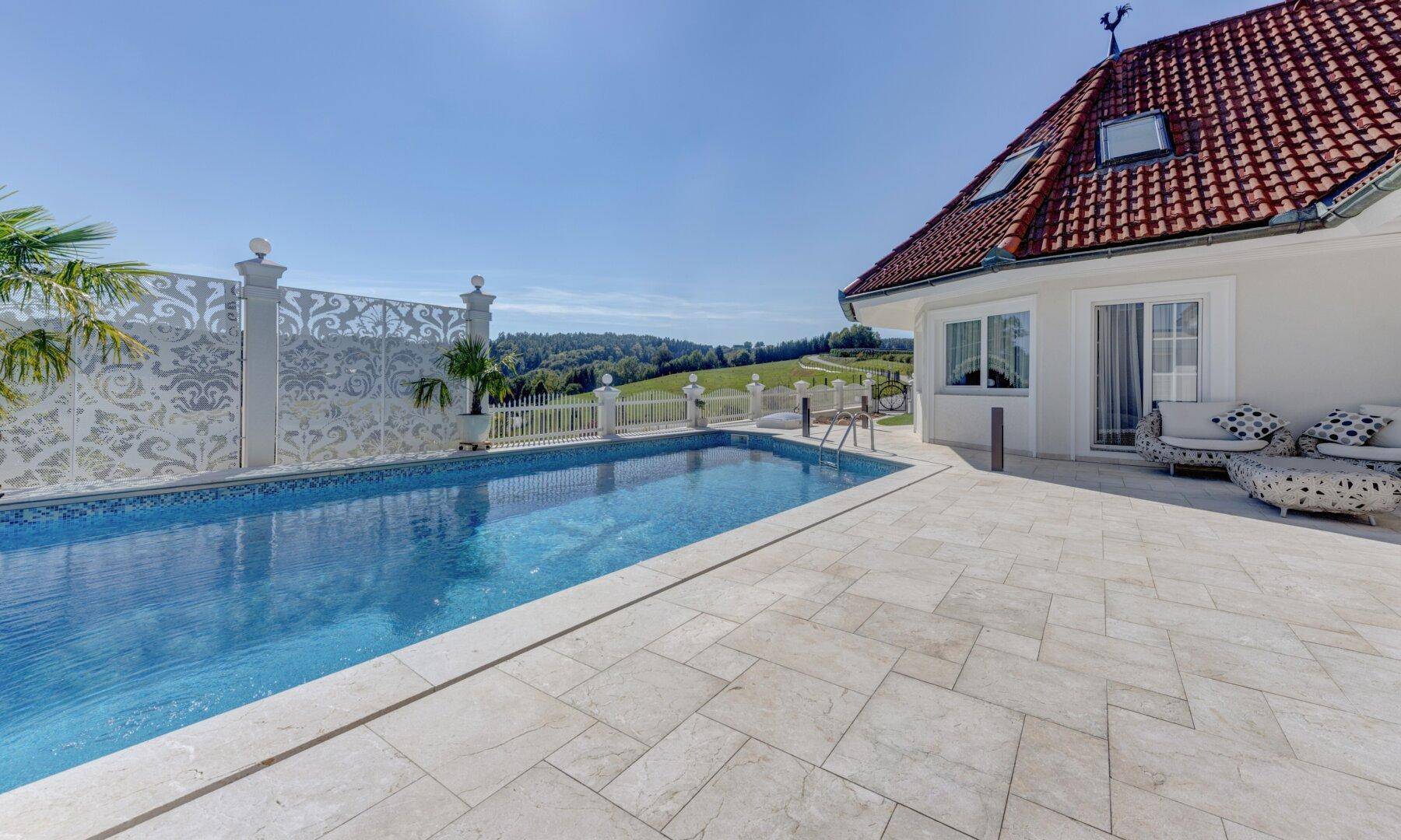 Poolbereich mit angrenzender Terrasse und Sitzgelegenheiten, umgeben von einer malerischen Landschaft.