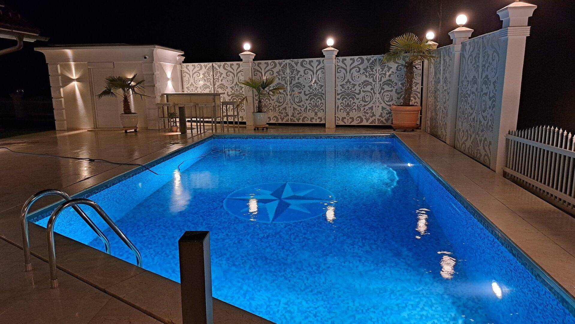 Der beleuchtete Poolbereich bei Nacht, mit einem Kompassstern-Muster am Boden.