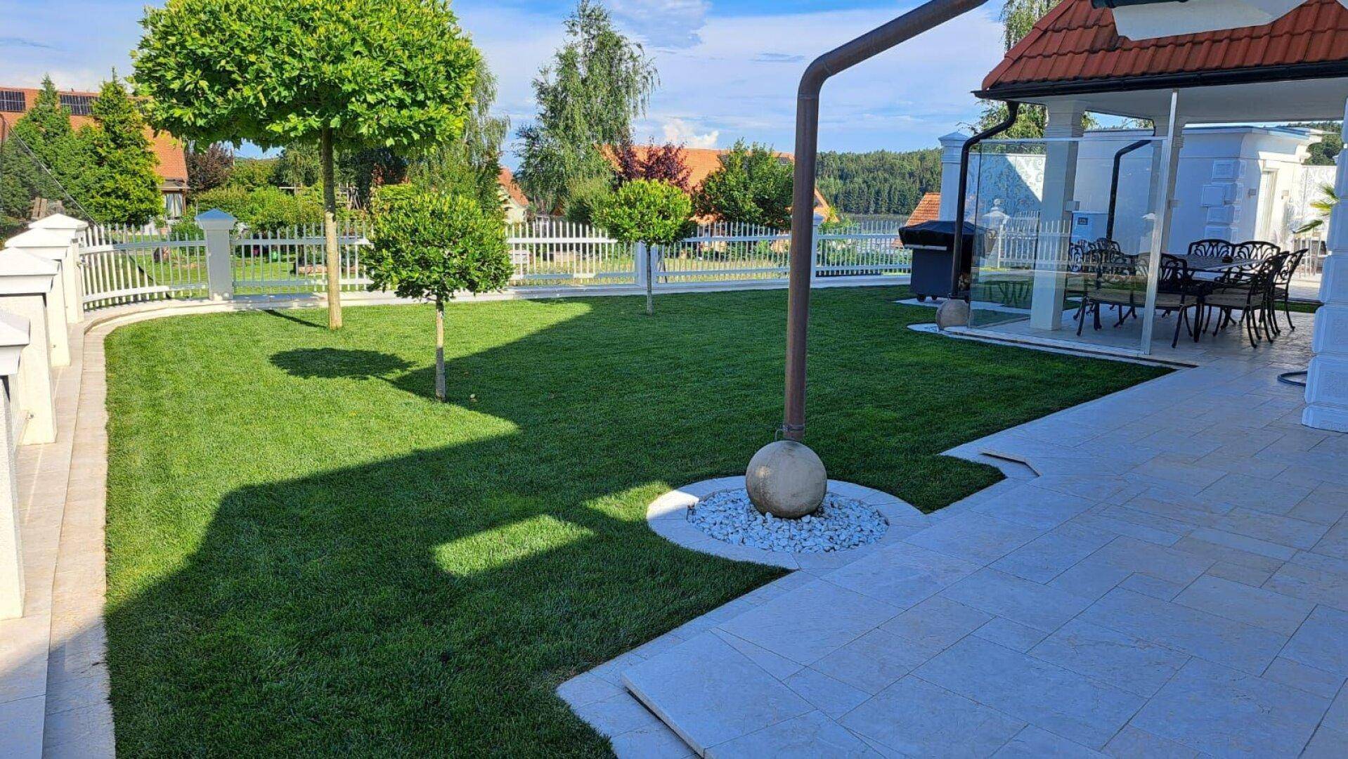 Gepflegter Rasenbereich mit Zierbäumen und einer Terrasse, ideal für Entspannung im Freien.