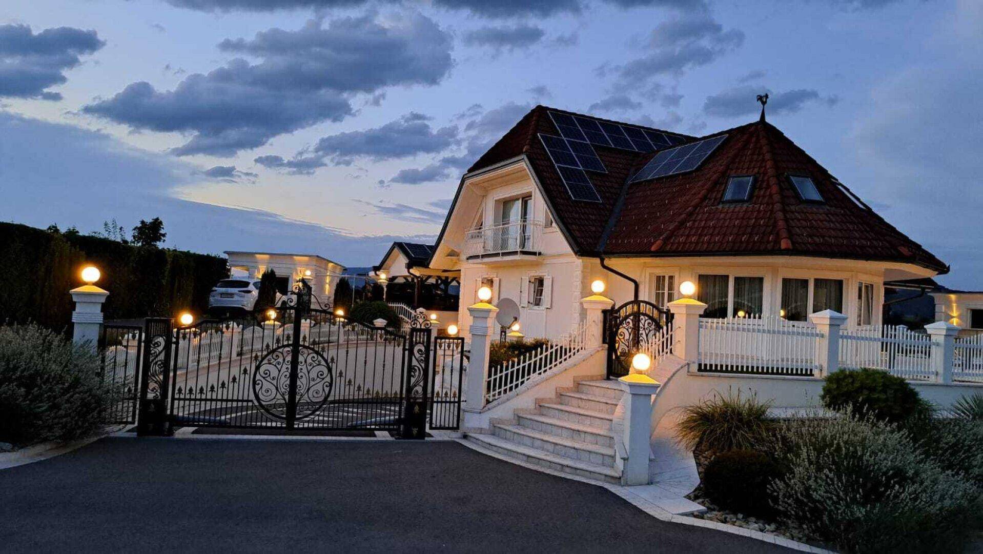 Das Anwesen bei Sonnenuntergang, beleuchtet von zahlreichen Außenleuchten, mit Solaranlagen auf dem Dach.