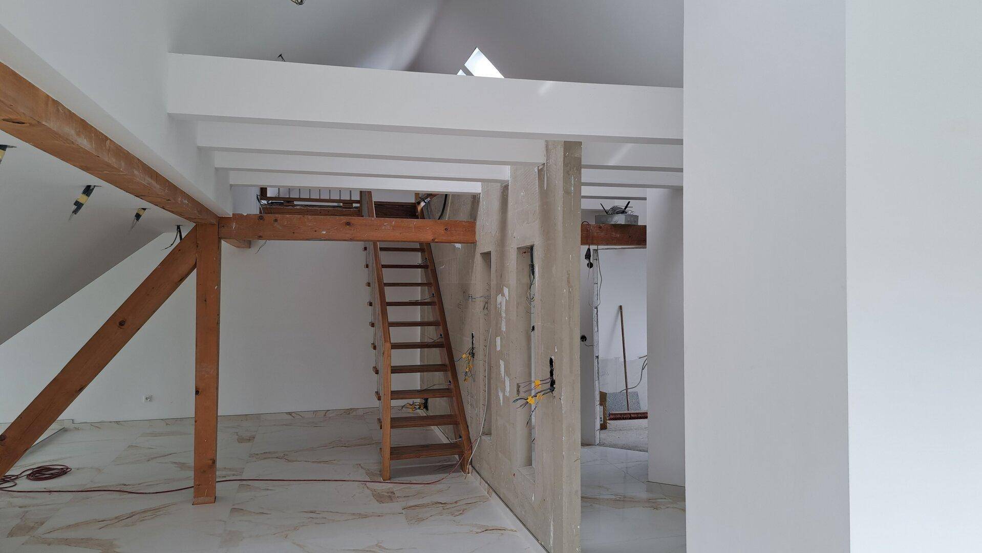 Unfertiger Dachbodenraum mit Holzbalken, Treppe und viel Potenzial.