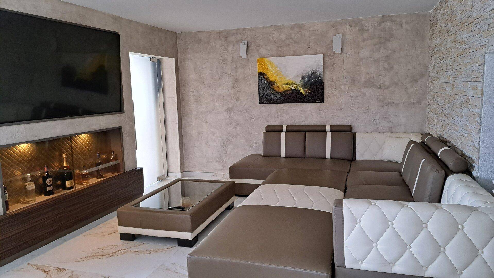 Modernes Wohnzimmer mit großem Ecksofa, Fernseher und beleuchteter Bar.