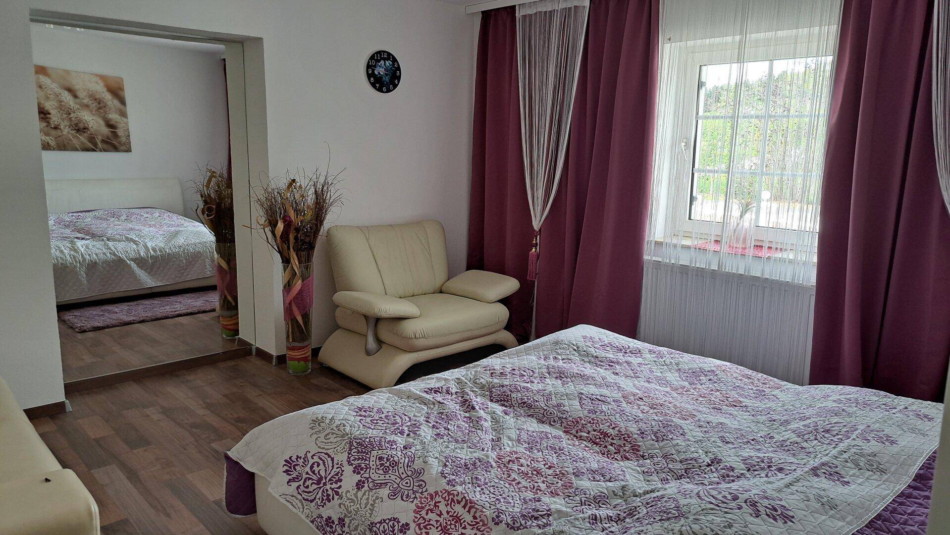 Gemütliches Schlafzimmer mit Holzboden, lila Bettwäsche und Blick in ein weiteres Zimmer.