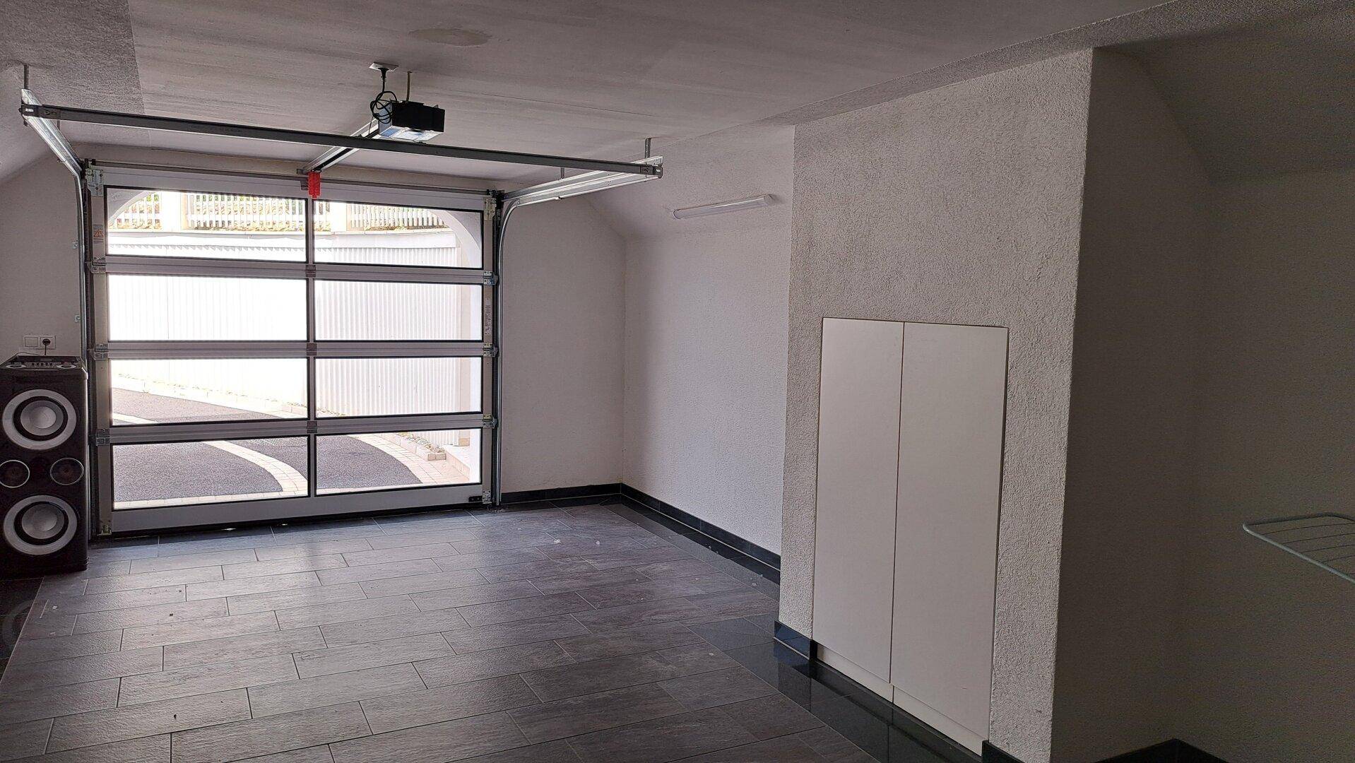 Geräumige Garage mit automatischem Tor, dunklem Fliesenboden und Stauraum.