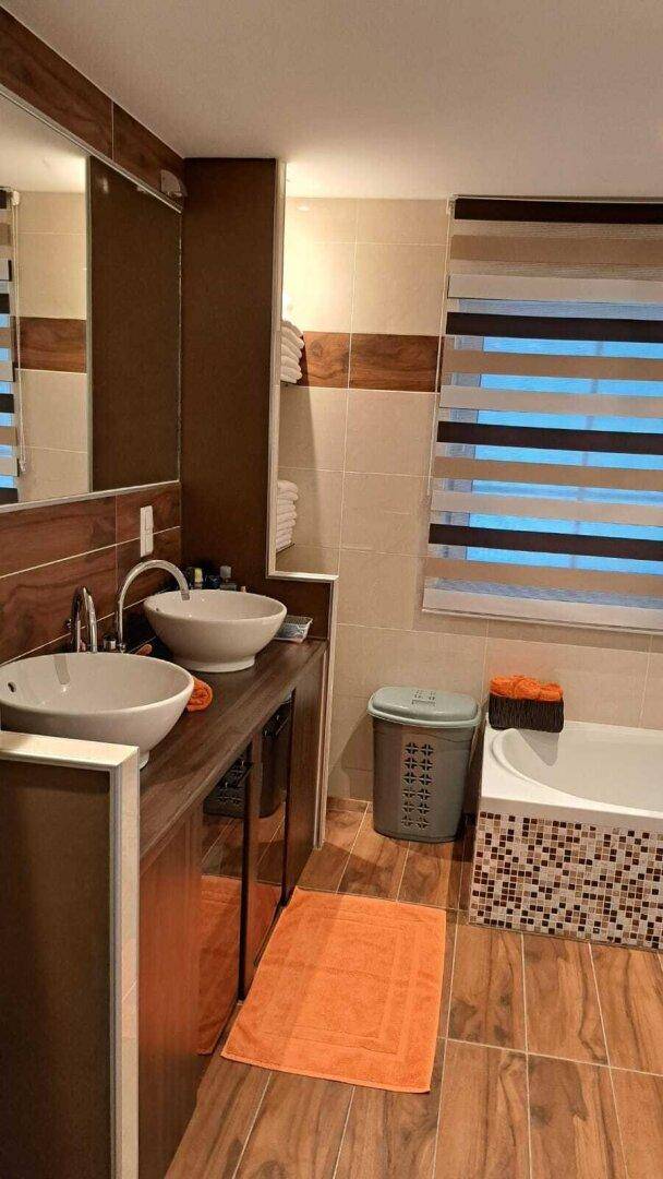 Modernes Badezimmer mit Doppelwaschbecken, Badewanne und Holzoptik-Fliesen.