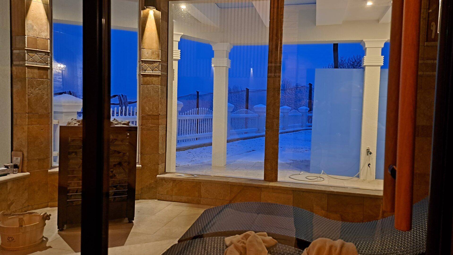Sauna mit Blick auf die winterliche Außenanlage bei Dämmerung.