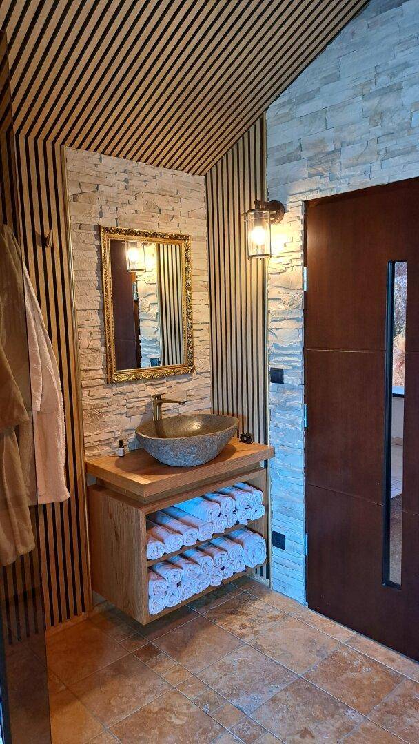 Modernes Badezimmer mit Steinwaschbecken, Holzlamellen und Steinwand.
