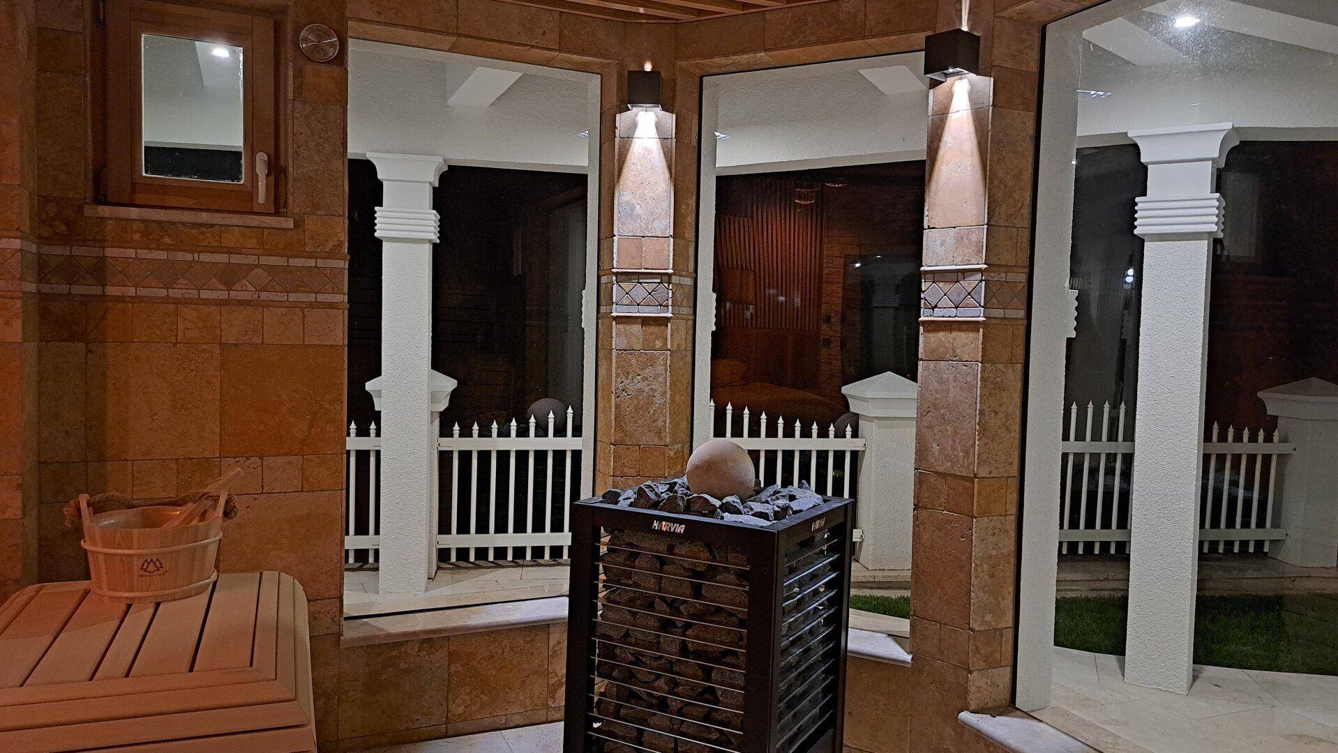 Sauna bei Nacht mit beleuchtetem Ofen und Blick auf die Außenanlage.