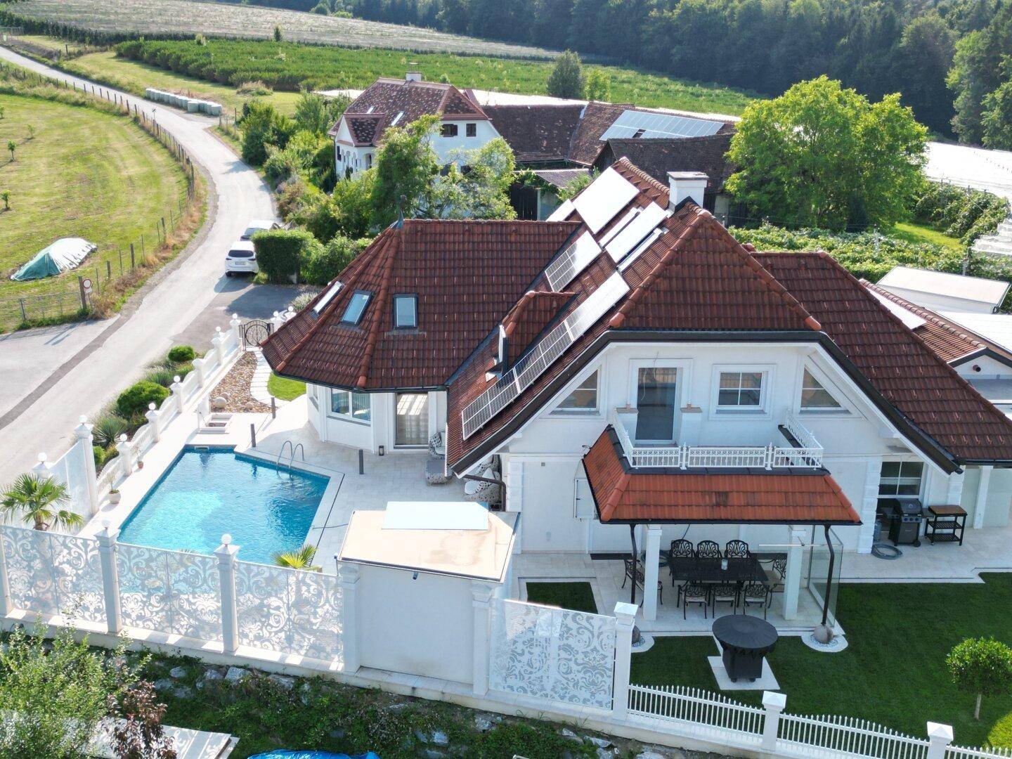 Ansicht des Hauses von der Seite mit Pool, Terrasse und Solaranlagen auf dem Dach, umgeben von Natur.
