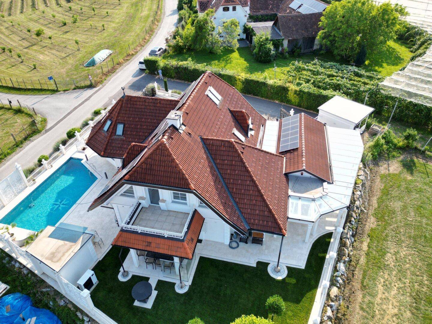 Luftaufnahme eines luxuriösen Hauses mit Pool, Terrasse und Solaranlagen auf dem Dach.