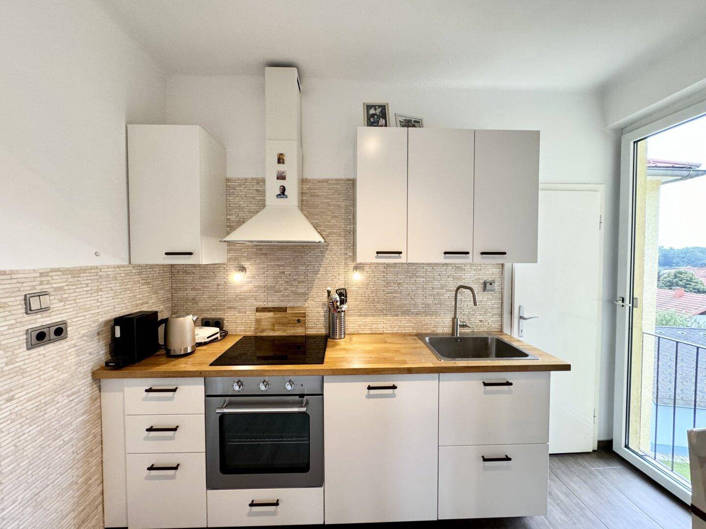 Detailansicht der modernen Küche mit Induktionskochfeld, Backofen und Zugang zum Balkon.