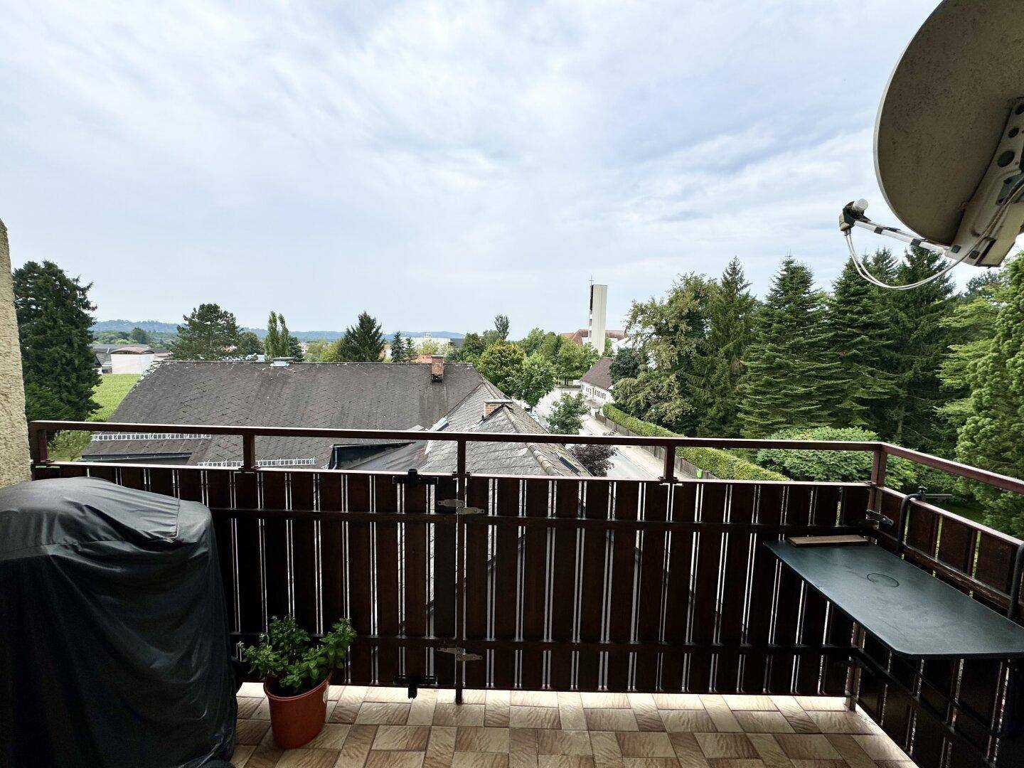 Balkon mit Fliesenboden, Holzzaun und Blick auf die umliegende Wohngegend und viel Grün.