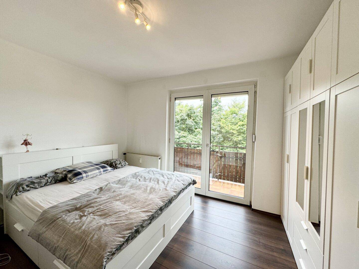 Schlafzimmer mit weißem Bett, großem Kleiderschrank und direktem Zugang zum Balkon.