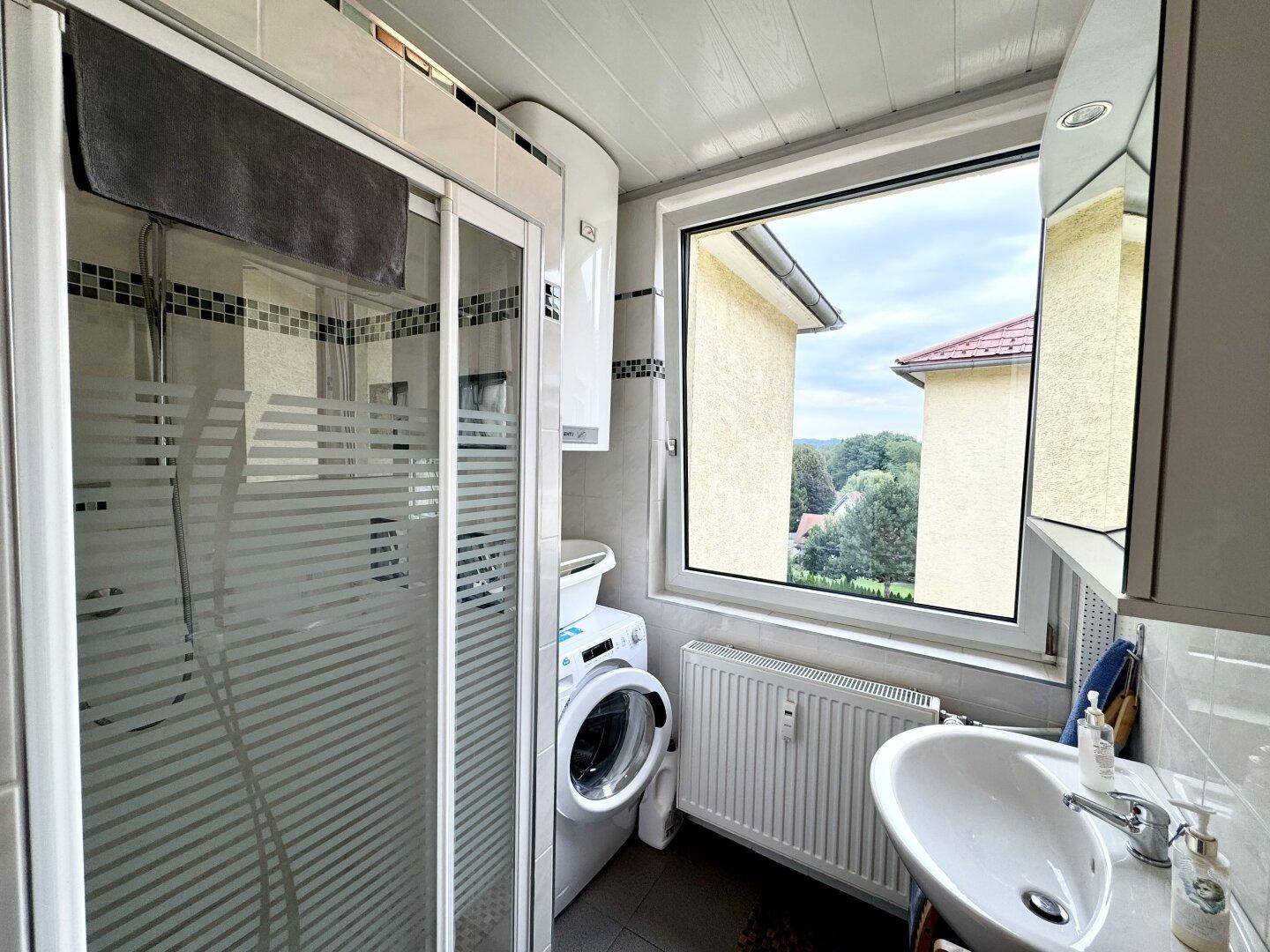 Badezimmer mit Duschkabine, Waschbecken, Waschmaschine und einem Fenster für Tageslicht.