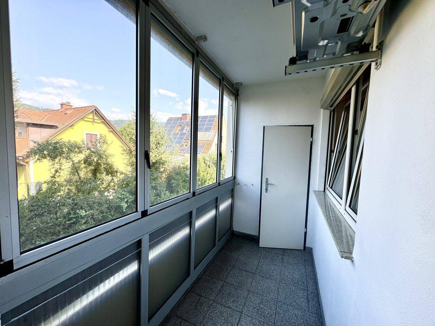 Verglaste Loggia mit Fliesenboden und Blick auf die umliegenden Häuser und Solaranlagen.