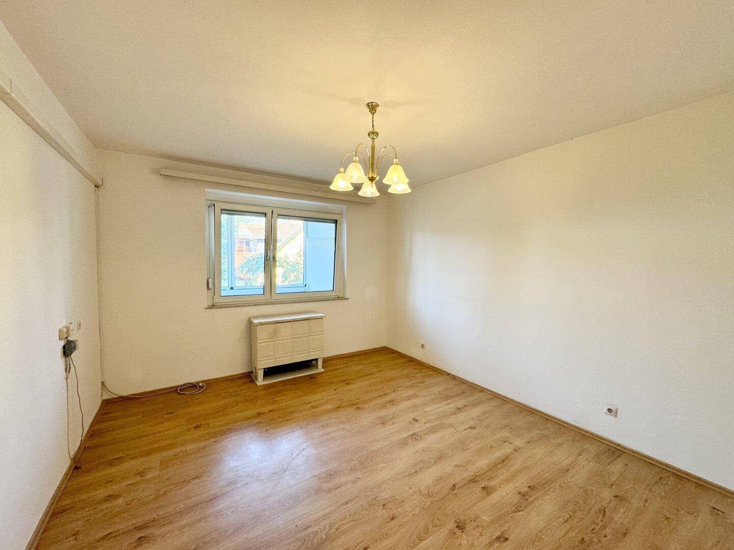 Helles Zimmer mit Laminatboden und einem klassischen Kronleuchter, ideal als Schlaf- oder Arbeitszimmer.