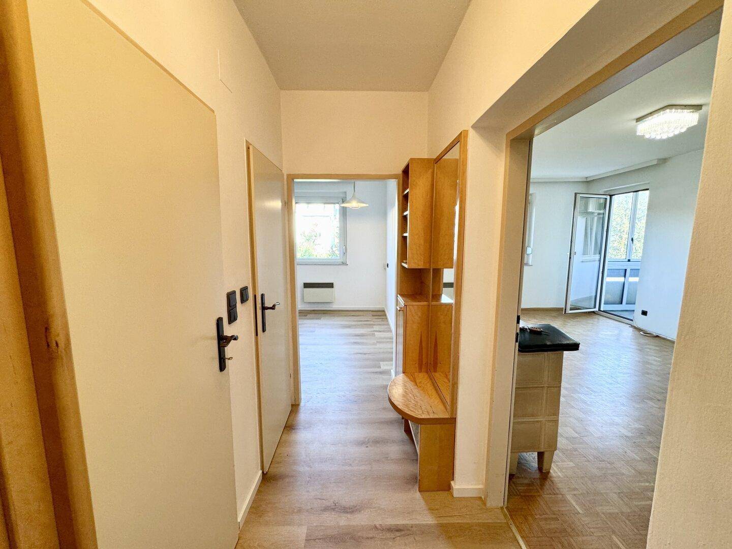 Heller Flur mit Laminatboden und einem dekorativen Holzregal, der zu weiteren Räumen führt.