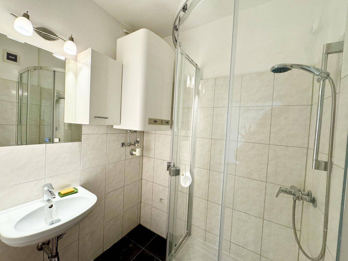 Funktionales Badezimmer mit Duschkabine, Waschbecken und weißen Fliesen, gut beleuchtet.