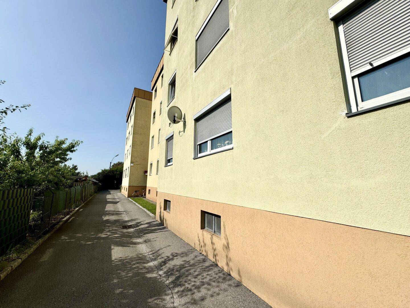 Seitenansicht eines Mehrfamilienhauses mit gelber Fassade und Rollläden an den Fenstern.