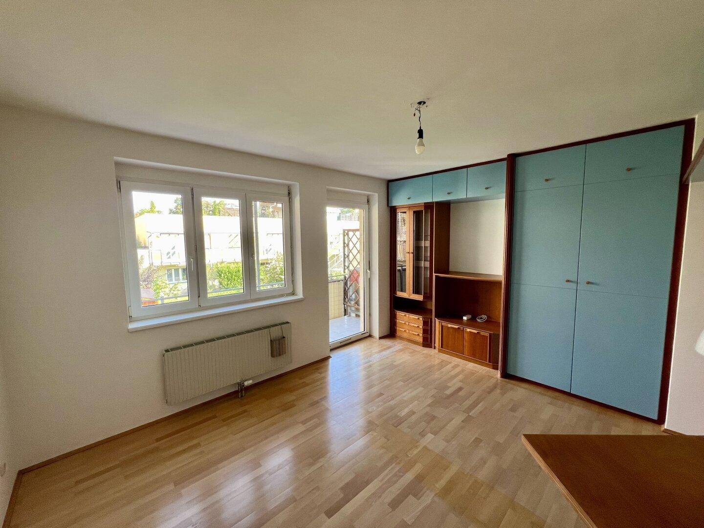 Helles Wohnzimmer mit Parkettboden, großen Fenstern und integrierten Schränken in Blau und Holz.