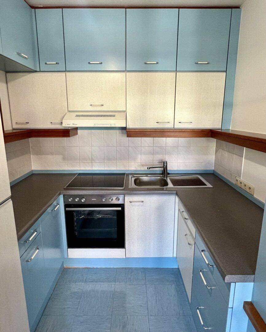 Funktionale Küche mit blauen und weißen Schränken, Fliesenboden und integrierten Geräten.