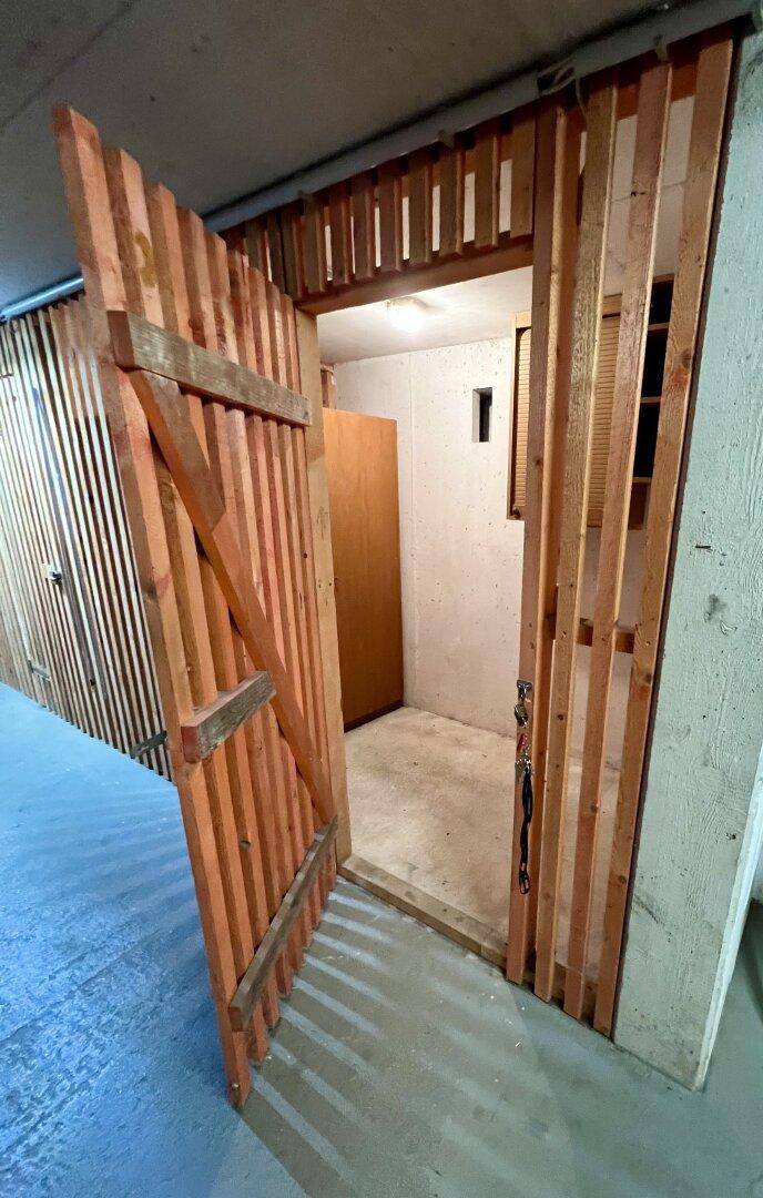 Kellerabteil mit Holztür und Betonboden, ideal für zusätzlichen Stauraum.