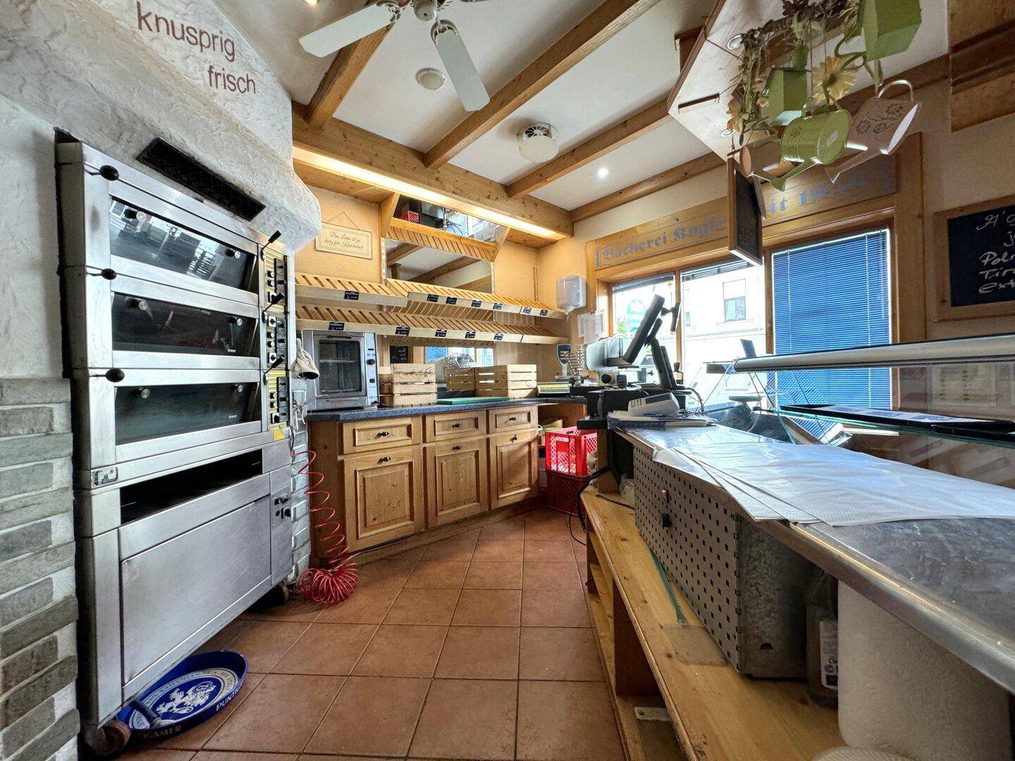 Backbereich der Bäckerei mit Öfen, Arbeitsflächen und Holzregalen im rustikalen Stil.